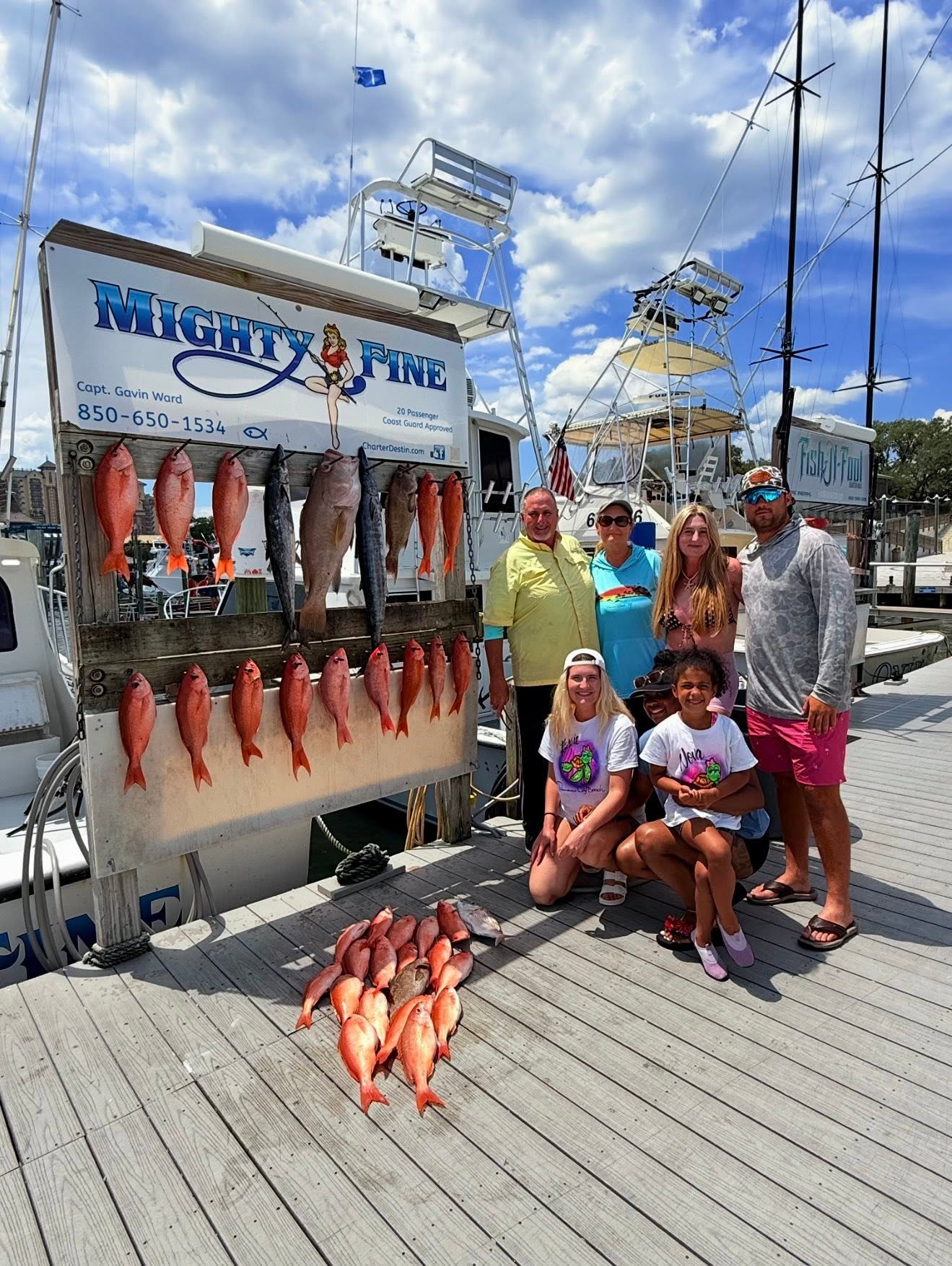 Family of seven at the dock with their catch of red snapper, king mackerel, and vermilion snapper on the Mighty Fine board