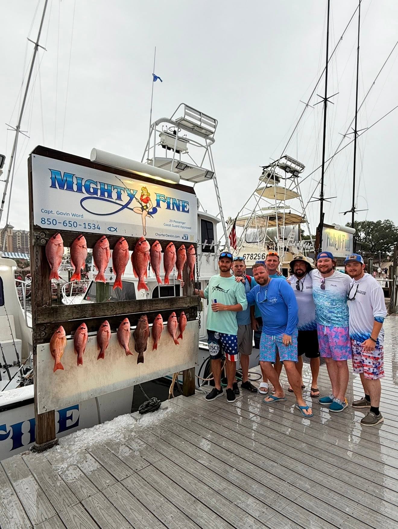 Seven friends beside the Mighty Fine catch board hung with a limit of red snapper and a row of vermilion snapper
