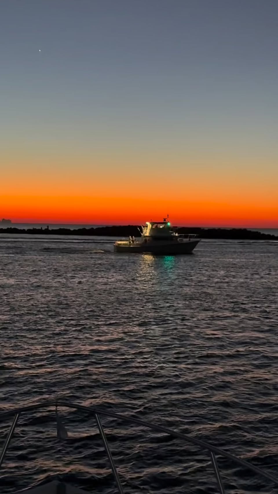 A charter boat passing the Destin jetties before dawn under a burning orange sky