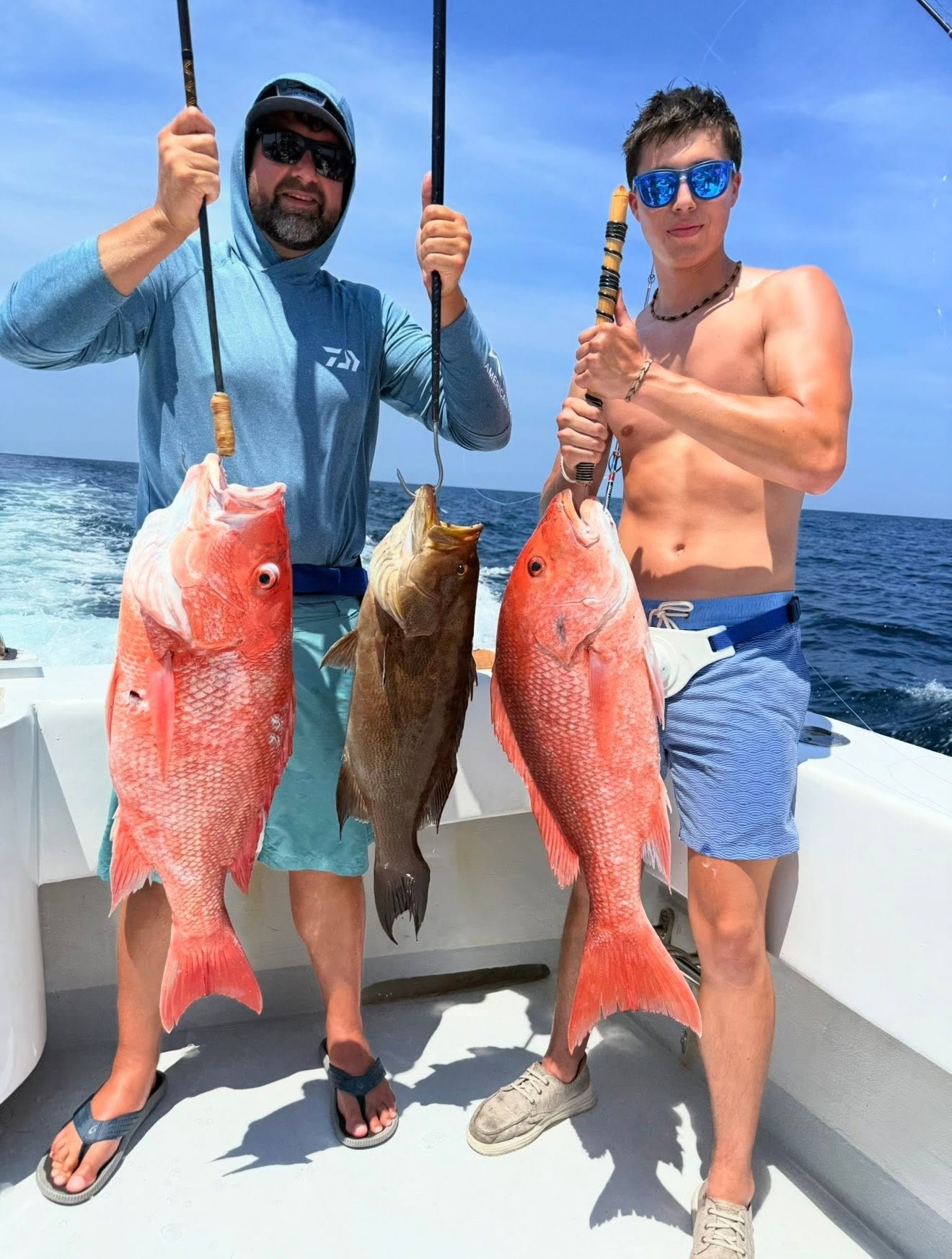 Two anglers holding big red snapper and a grouper in bright midday sun
