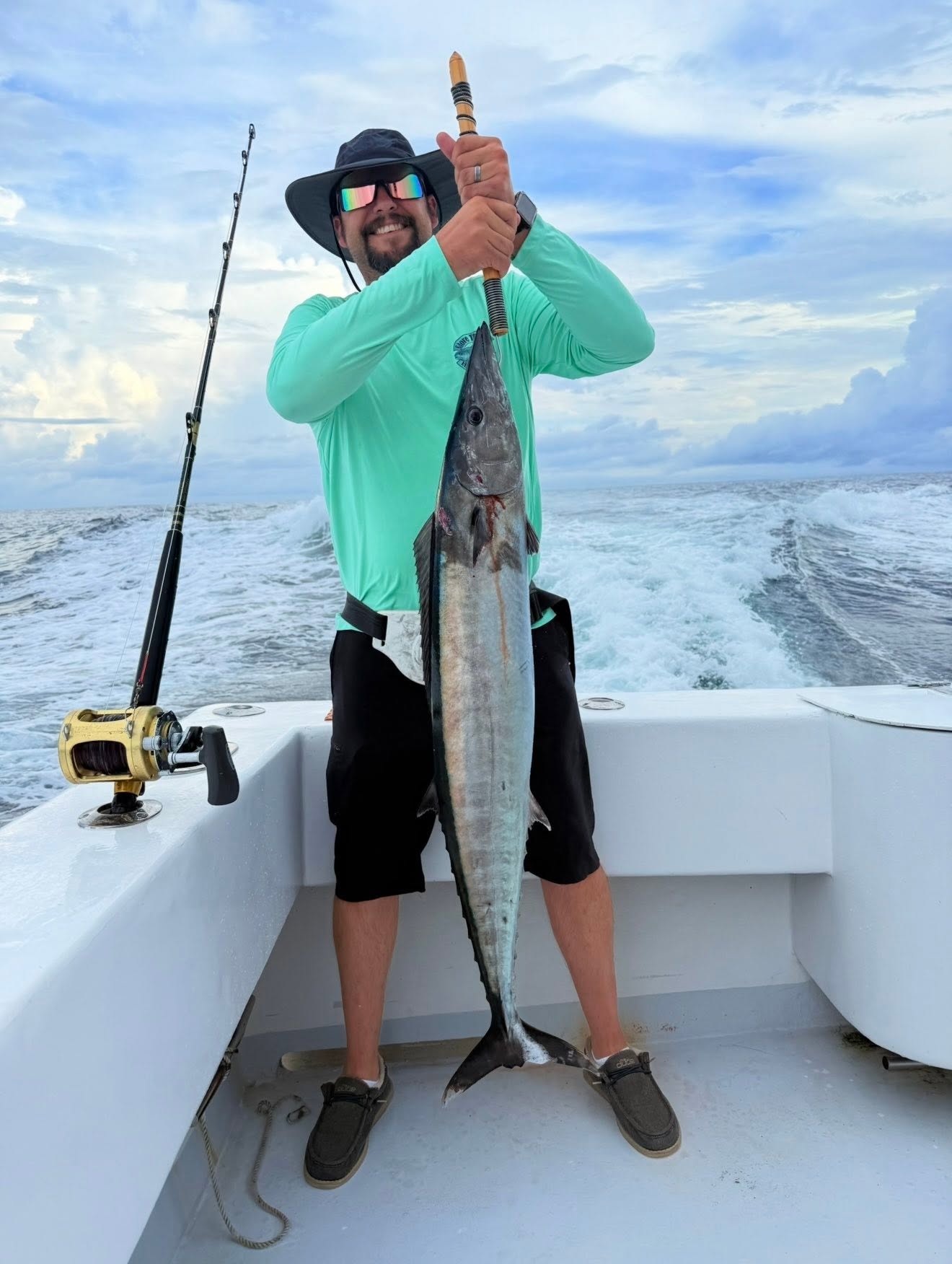 Angler in a sun hat holding a large wahoo at the stern of the boat